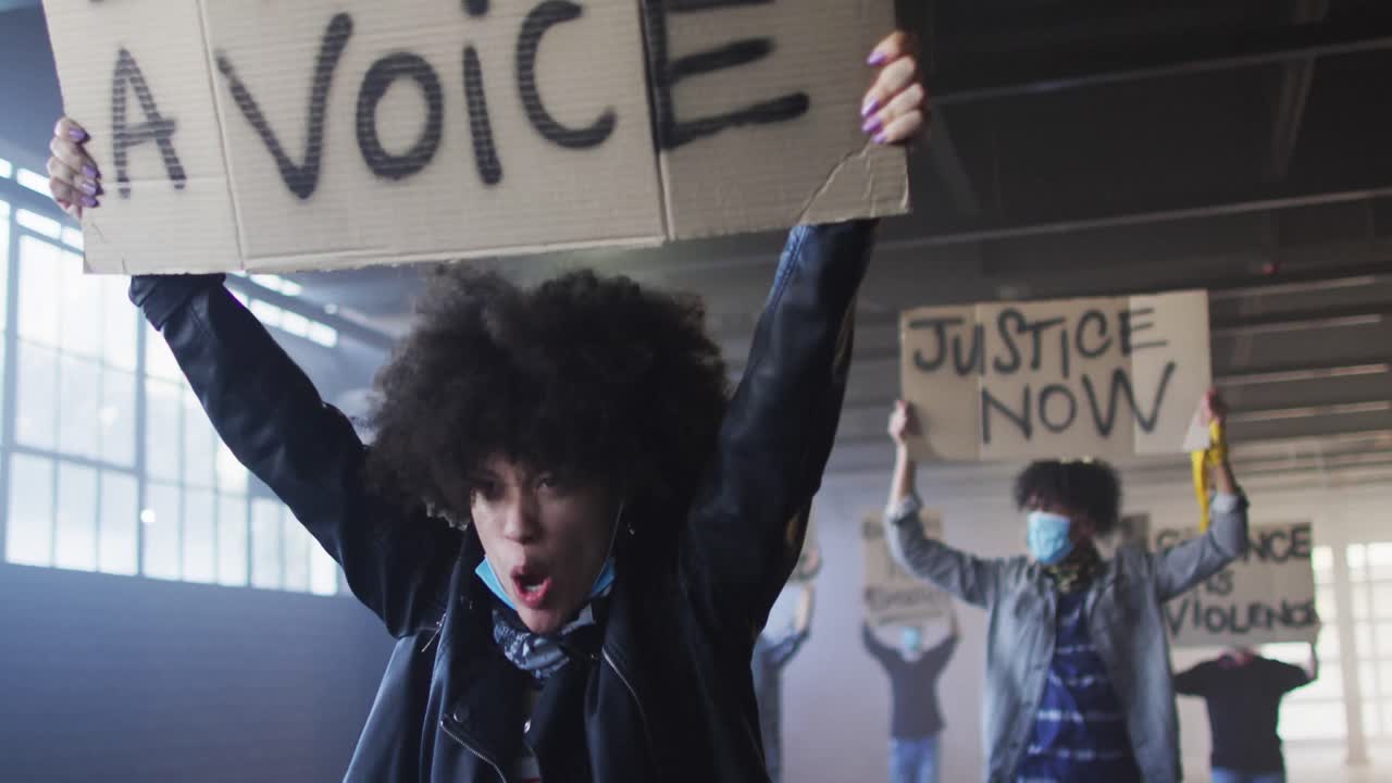 разнообразная группа людей в масках с плакатами протеста, кричащими, поднимающими кулаки