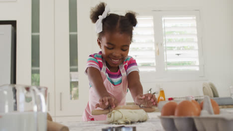 Happy-african-american-girl-rolling-dough-in-kitchen