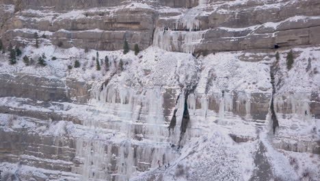 a frozen waterfall along a rugged cliff with mountain climbers at the base of the ice climbing up - zooming out