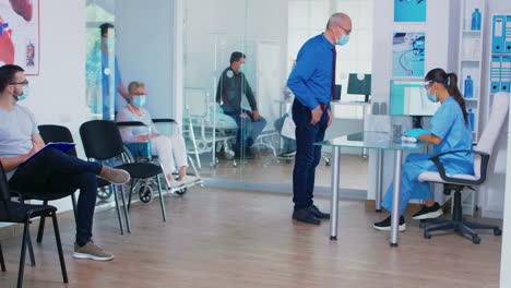 Senior-man-discussing-with-nurse-at-hospital-reception