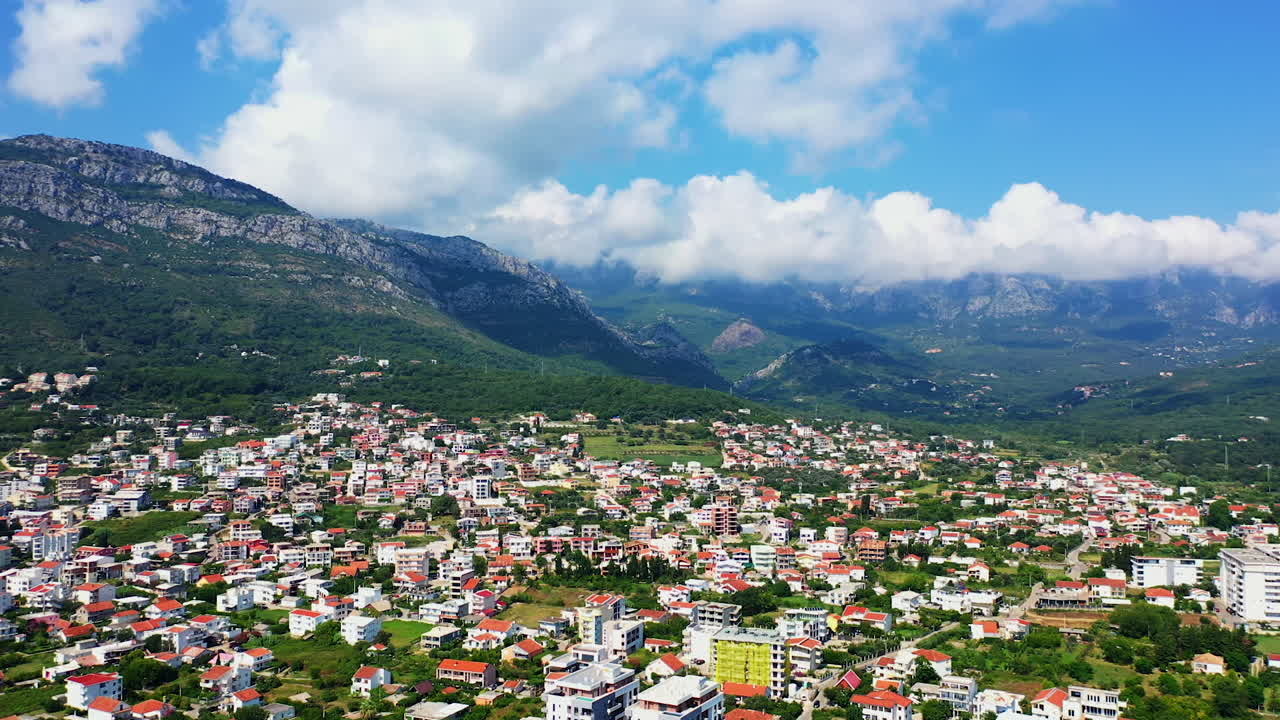 Densely built low architecture of the city of Bar in Montenegro. White cloudscape covering the tops of the mountains surrounding the city. Aerial view.
