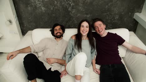 friendship, new home concept - smiling male and female friends are falling on the new white sofa together, front high angle view