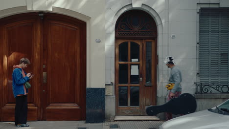 man with guitar in case walking and entering house