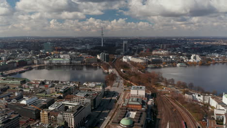 Wide-aerial-view-of-car-and-train-traffic-across-Binnenalster-lake-with-Hamburg-panorama-in-the-background