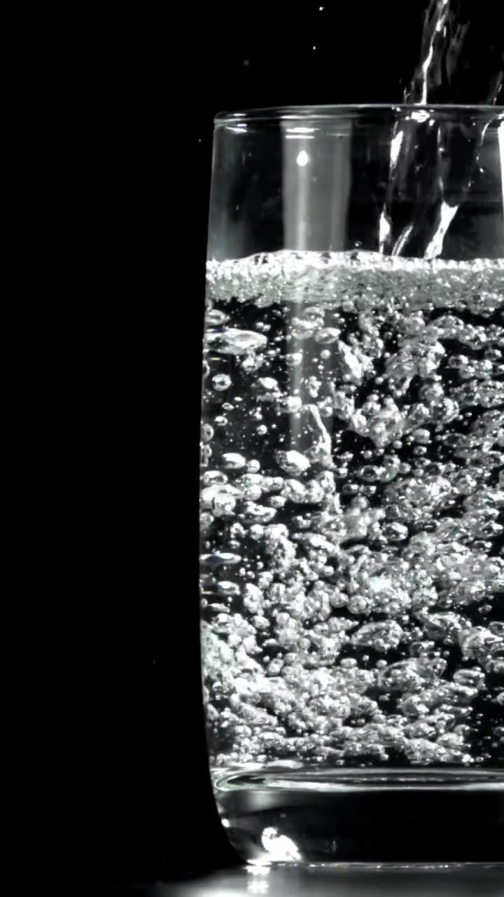 Acqua trasparente versata in un bicchiere con bollicine su sfondo nero