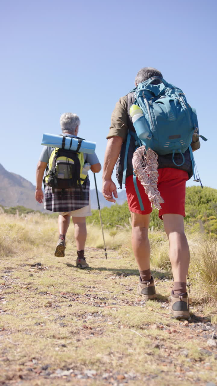 Vertical video of senior biracial couple hiking in mountains, in slow motion