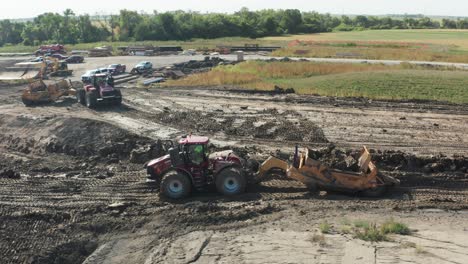 Aerial,-tractor-pulling-trolley-trailer-full-of-soil-driving-on-rural-construction-site