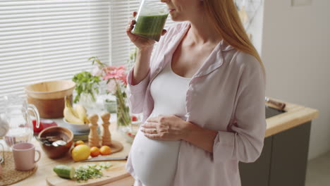 pregnant woman drinking green smoothie in kitchen