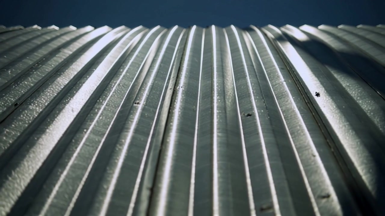 Oggetto in movimento che proietta un'ombra curva che si estende su un pannello metallico sul bordo del tetto, rivelando gli elementi di fissaggio.