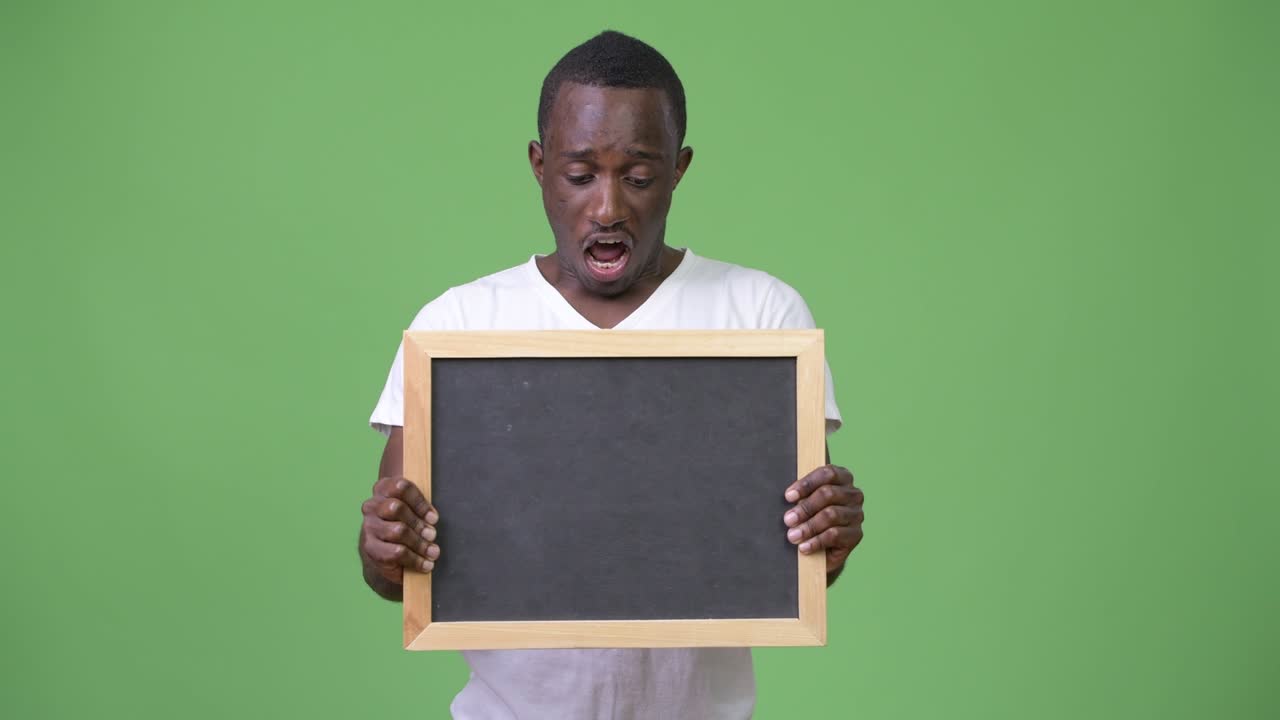 Young African man showing blackboard and looking shocked