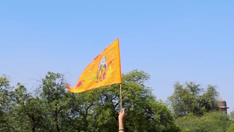 Bandera-Sagrada-De-Azafrán-Con-El-ídolo-De-Lord-Rama-Agujereado-En-La-Mano-Con-Fondo-De-Cielo-Azul-Brillante-Durante-El-Día