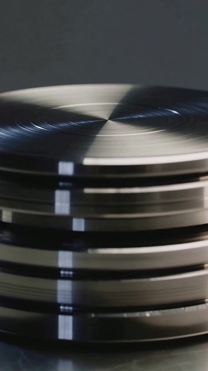 Vertikales Video: Rotierender bearbeiteter Metallpuck dreht sich auf Tischplatte im Studio, zeigt seitliche Rillen.