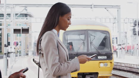 businesspeople commuting to work standing on train platform using mobile phone as train arrives