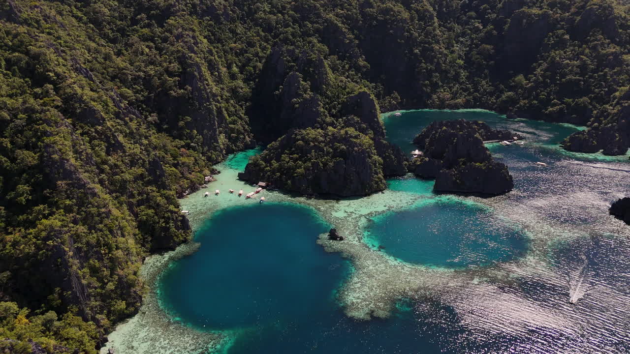 Aerial footage of Philippines Coron Island’s tropical beauty, with its dramatic cliffs, pristine beaches, and turquoise waters. Rotating drone shot with boats in the harbor.