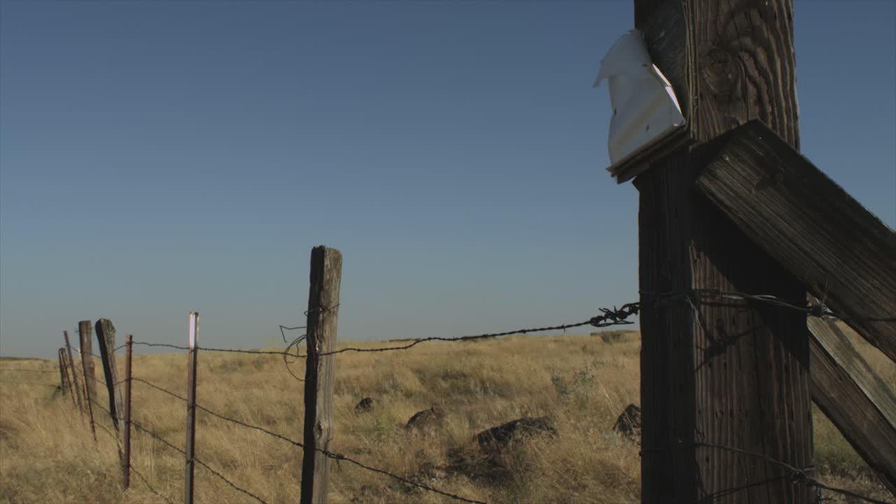 dry desert rocky grassland landscape. barbed wire fence going off into the distance with a piece of paper stapled to it