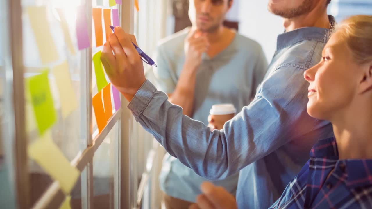 Video di colleghi e colleghe creativi e diversi che scrivono su post-it in un ufficio moderno