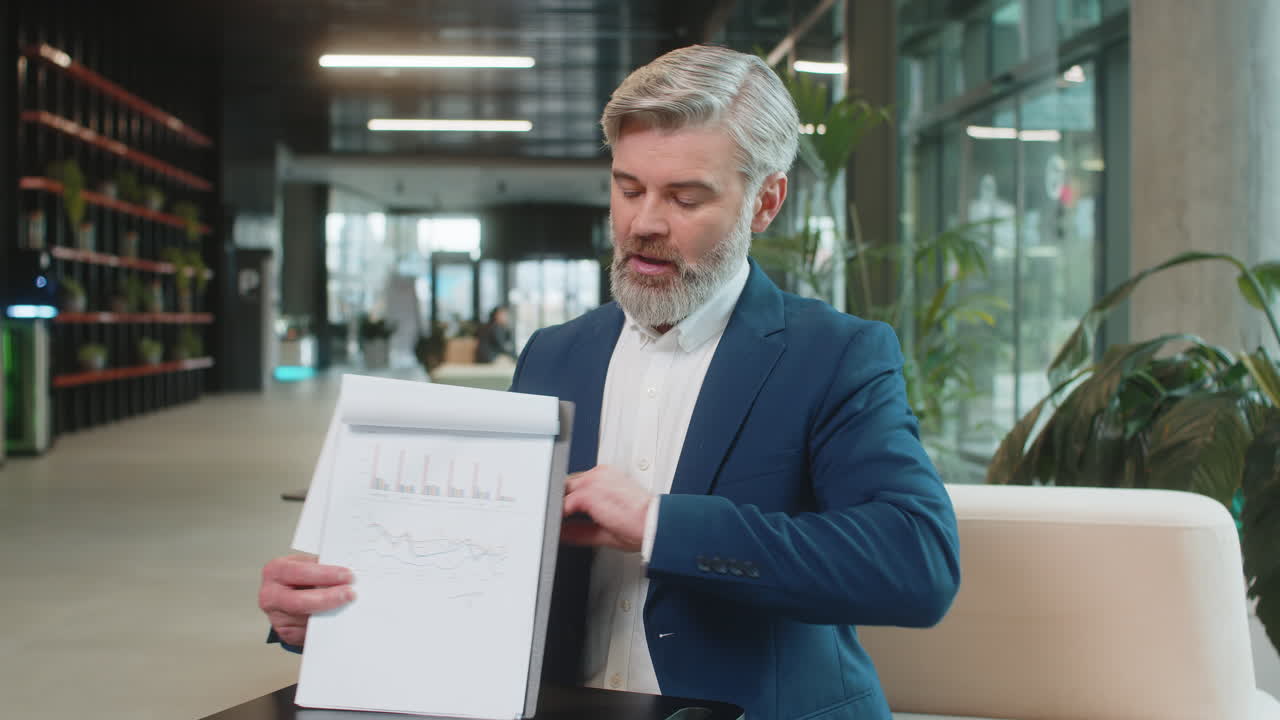 Mature businessman making online presentation video call demonstrates reports in office lobby