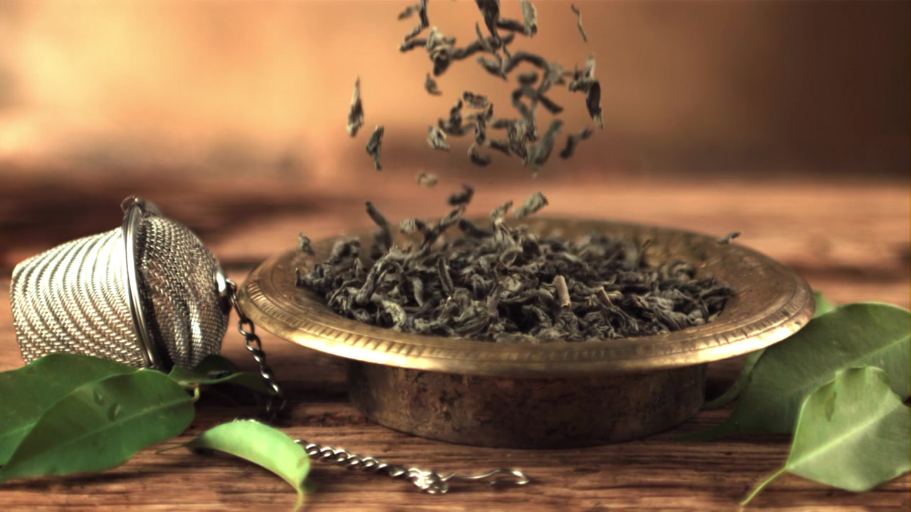 Dried Green Tea Leaves Falling into a Brass Bowl with Infuser