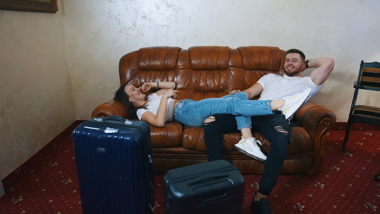 Man and woman rest on a couch tired from journey. Young couple lying on sofa waiting for the leaving the hotel on suitcases packed background.