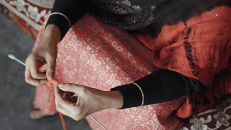 woman siting on bed and knitting with red wool