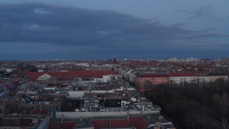 Establisher-shot-of-rooftop-of-traditional-brick-houses-across-street-surrounded-with-trees-on-a-cloudy-early-morning-in-Berlin,-Germany