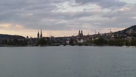 Vergrößerte-Aufnahme-Einer-Tief-Fliegenden-Drohne,-Die-Bei-Sonnenuntergang-über-Dem-Zürichsee-In-Richtung-Stadt-Fliegt