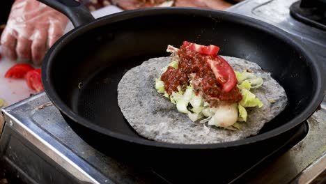 cooking chicken taco series: close-up of chef's hand wearing gloves slicing and putting green bell pepper onto flour tortilla in a frying pan