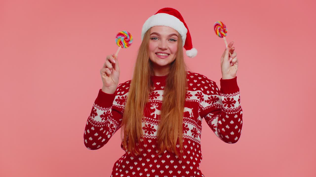 Funny girl in new year sweater holding candy striped lollipops hiding behind them fooling around