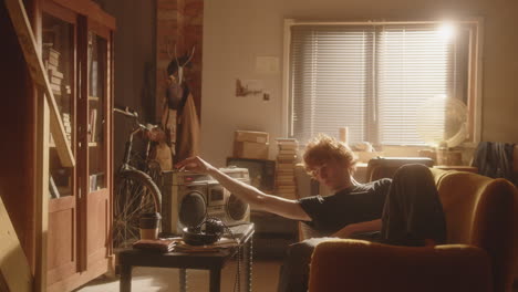 melancholic young man lounging on sofa at home, listening to music on boombox