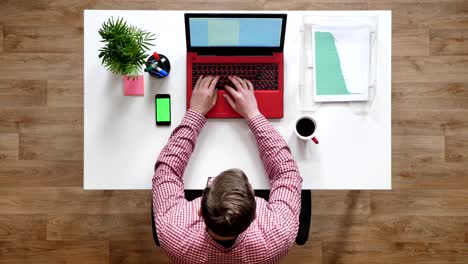 young man in glasses typing on laptop, topshot, sitting behind desk, phone with chroma key