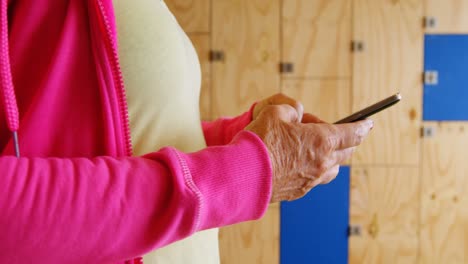 mujer mayor usando teléfono móvil en el vestuario del gimnasio 4k