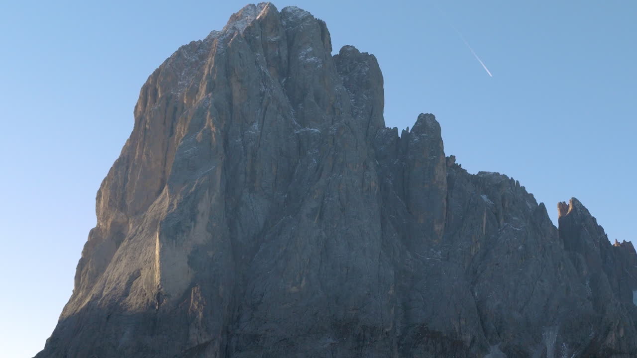 Cinematic aerial view of the Dolomites in Italy, rugged alpine peaks glowing at dawn, dramatic cliffs and deep shadowed valleys creating a serene high-altitude mood