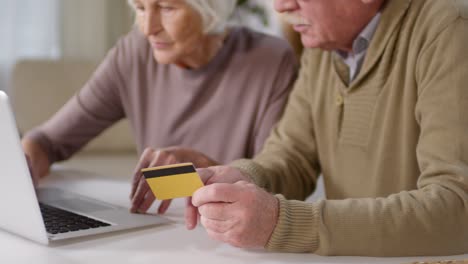 casal de idosos fazendo pagamento online usando cartão de crédito e computador portátil