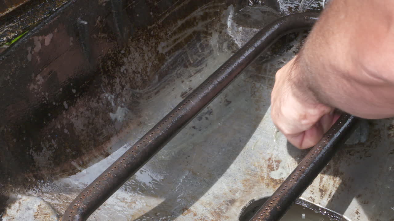 Slow motion footage of a man's hand scrubbing a filthy barbeque grill with a steel wool cleaning pad
