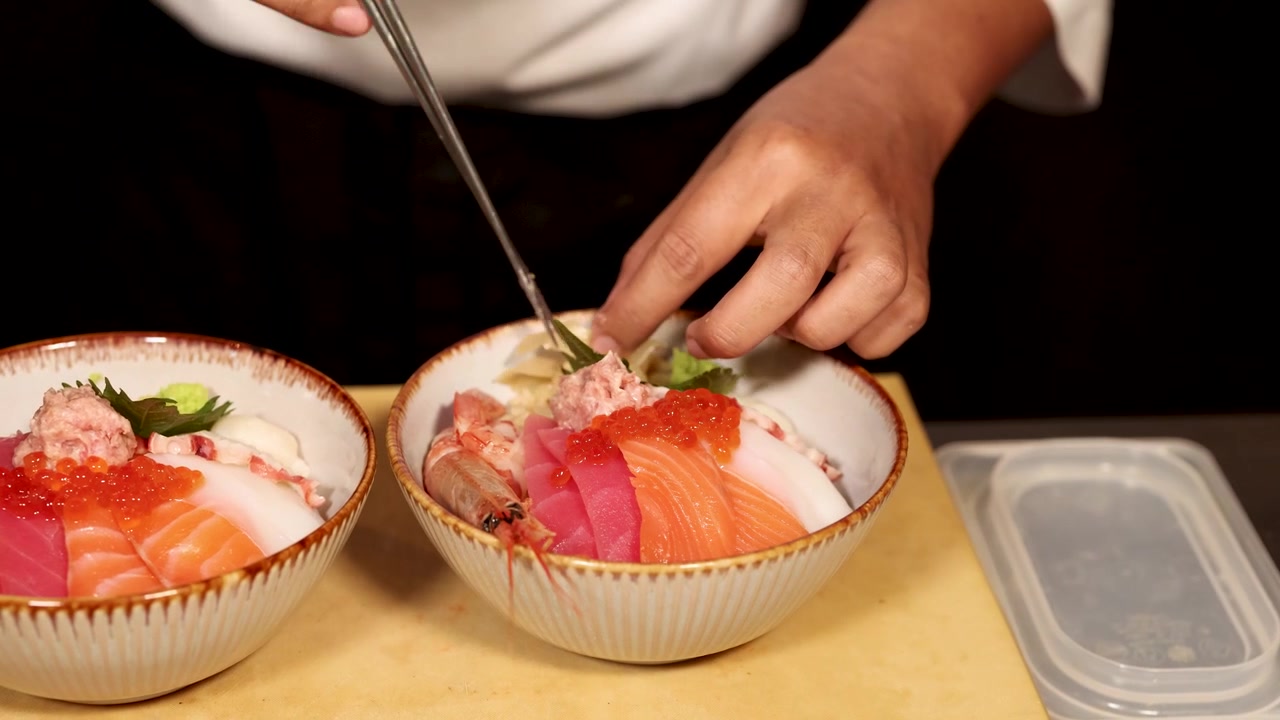 レストランでシェフが箸を使い、新鮮な海鮮丼に生姜とわさびを添えて盛り付けている