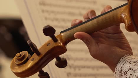 Nahaufnahme-Der-Geige.-Beherrschung-Geschickter-Hände-Beim-Spielen-Des-Instruments,-Wobei-Der-Schwerpunkt-Auf-Dem-Wirbel-Liegt,-Inmitten-Einer-Symphonie-Aus-Notennoten