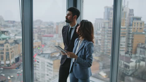 two company employee talking work tasks at office window. couple colleagues