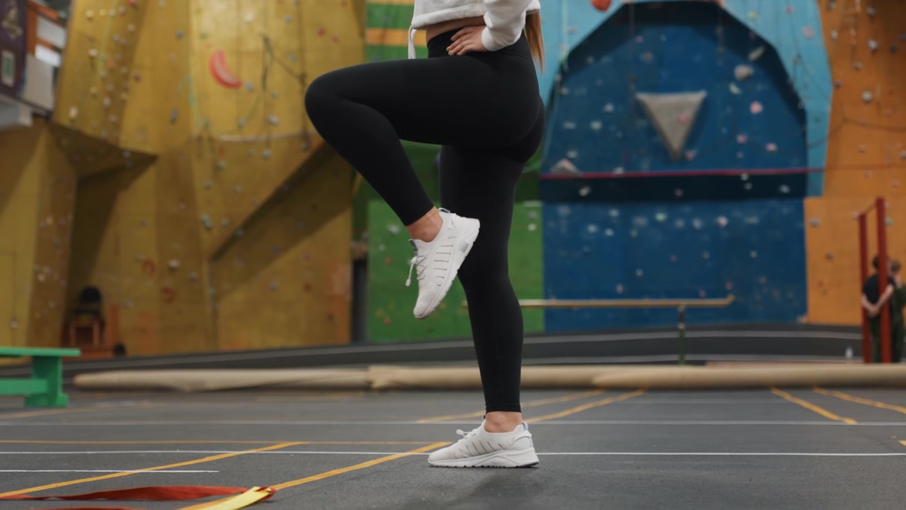 Secuencia progresiva de juego de pies en cancha cubierta para el desarrollo de habilidades de bádminton, el atleta practica el equilibrio controlado sobre una pierna, cambios de ritmo, aterrizajes precisos y trabajo de estabilidad cerca de un rocódromo.