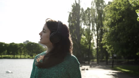 attractive young italian woman with headphones listening to music at the park with a sunset look around smile, dancing, enjoying life