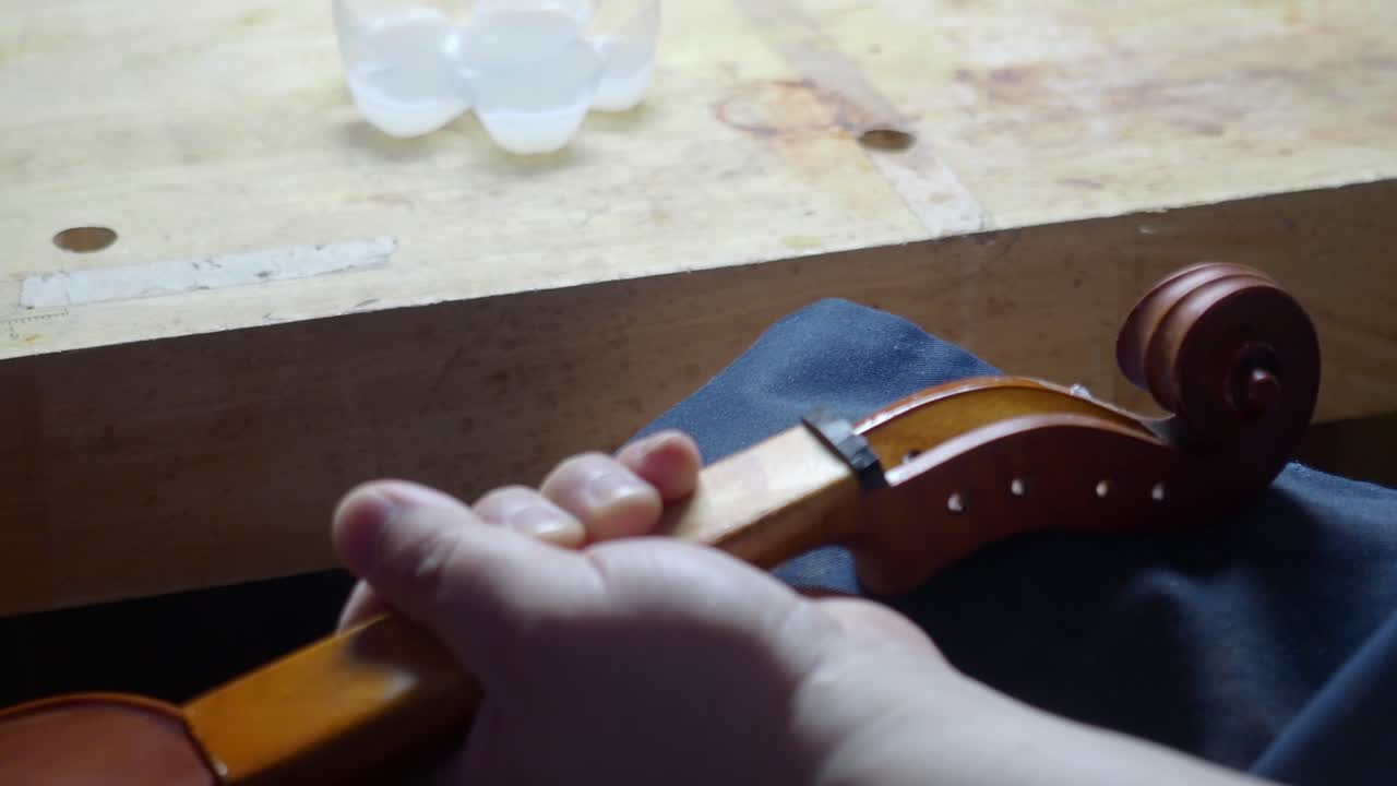 master artisan luthier violin maker antiquize violin curl and peg box with cloth and acid caustic oil on new stringed instrument to reproduce original masterpiece distress