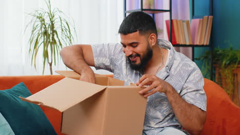 Happy-Arabian-man-shopper-unpacking-cardboard-box-delivery-parcel-online-shopping-purchase-at-home