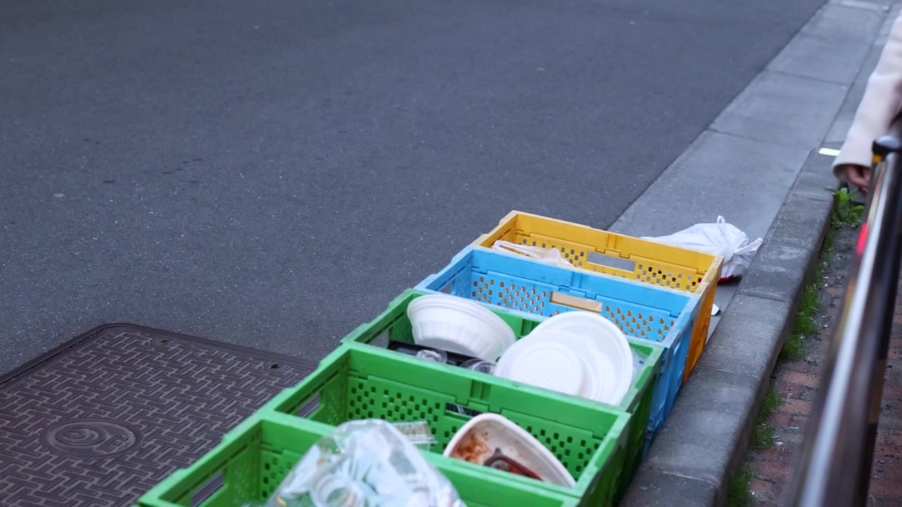 Close-up of hand discarding waste into colorful plastic bins on a Tokyo street sidewalk.