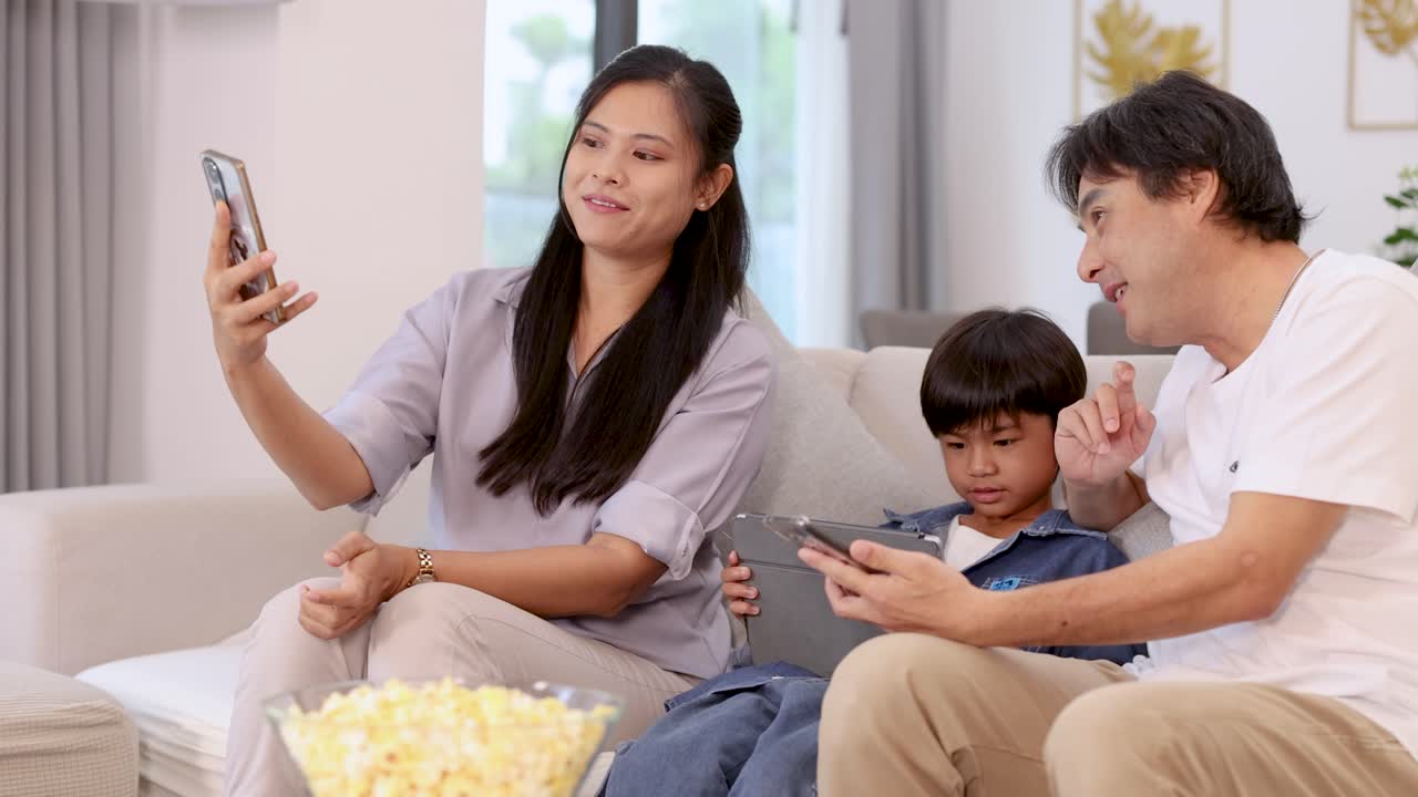 Happy family taking selfies together on sofa in bright, cozy living room, enjoying quality time