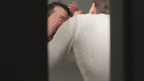 man examining receding hairline in a bathroom mirror, concern visible, in natural light