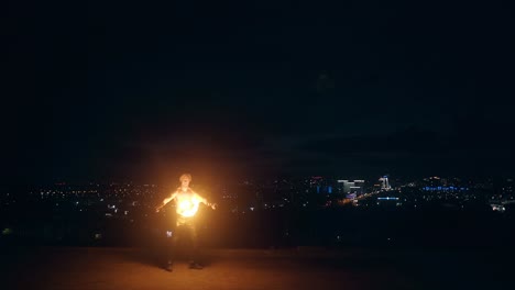 young blond male plays with two fire torches spins them at night on black background