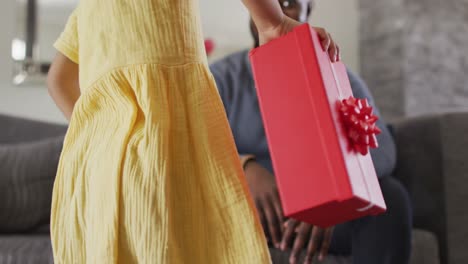 hija afroamericana dando regalo al padre sorprendido