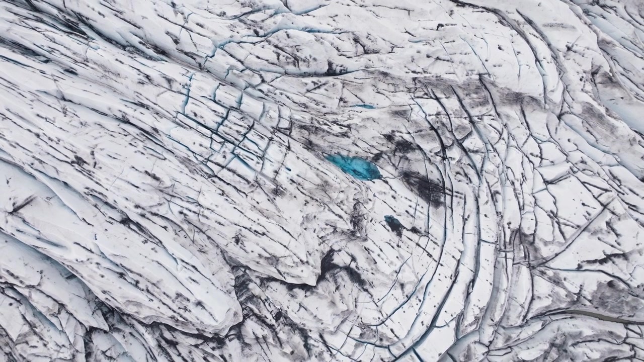 Acqua limpida e blu intrappolata in una pozza glaciale circondata da striature di cenere scura. Vista aerea.