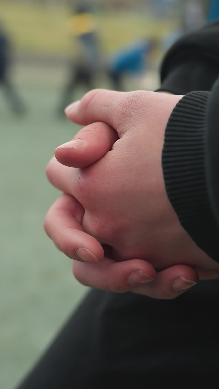 Close-up of someone's hands clasped together with a blurred view of children playing in the background