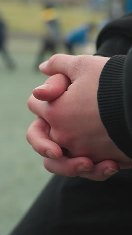 close-up of someone's hands clasped together with a blurred view of children playing in the background