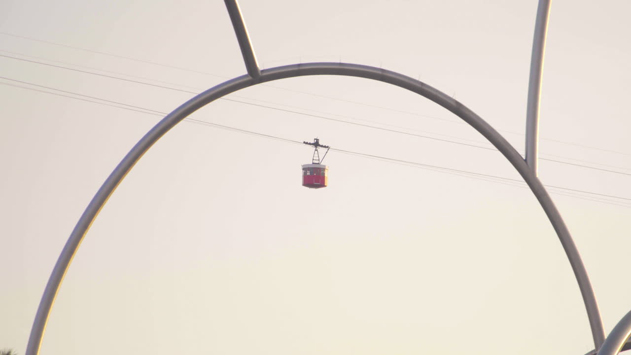 Red cable car passes over Barcelona sailboat bay view at sunset in January